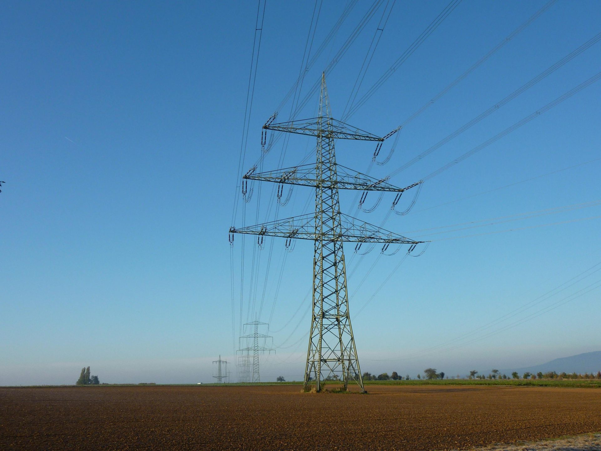 Hochspannungsleitungen an einem Turm, der auf einem offenen Feld vor klarem, blauem Himmel steht.
