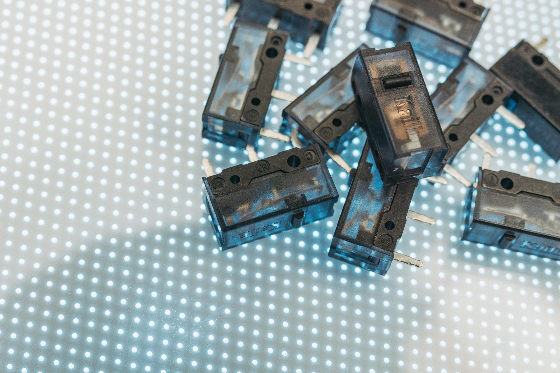 Makroaufnahme von schwarzen elektronischen Schaltern auf einer beleuchteten LED-Oberfläche, die die technischen Komponenten hervorhebt.